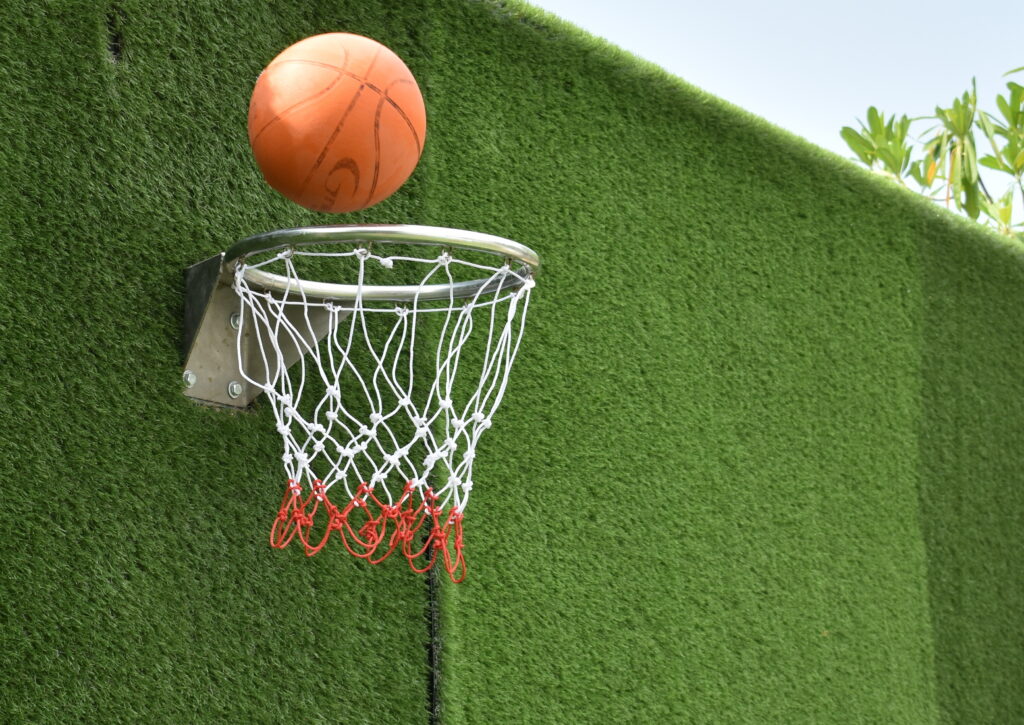 Depositphotos_346704322_XL Basketball flies towards hoop against green wall, highlighting outdoor game and sports action. | Sky Rye Design Basketball flies towards hoop against green wall, highlighting outdoor game and sports action.