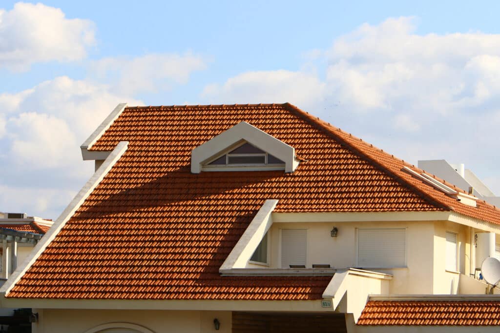 Modern house with red tile roof under blue sky, featuring windows and a small balcony.
