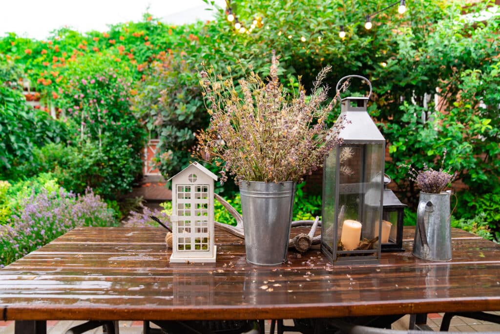 Outdoor table with lavender arrangement and lanterns, surrounded by lush garden and string lights.