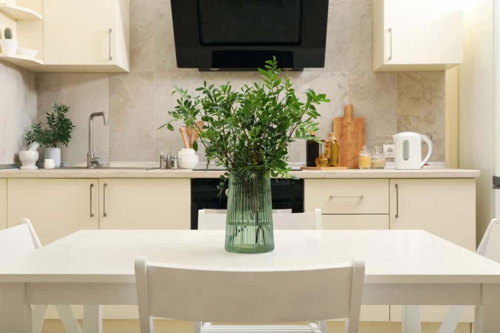 Modern kitchen with white cabinets and a dining table featuring a green vase of fresh greenery.