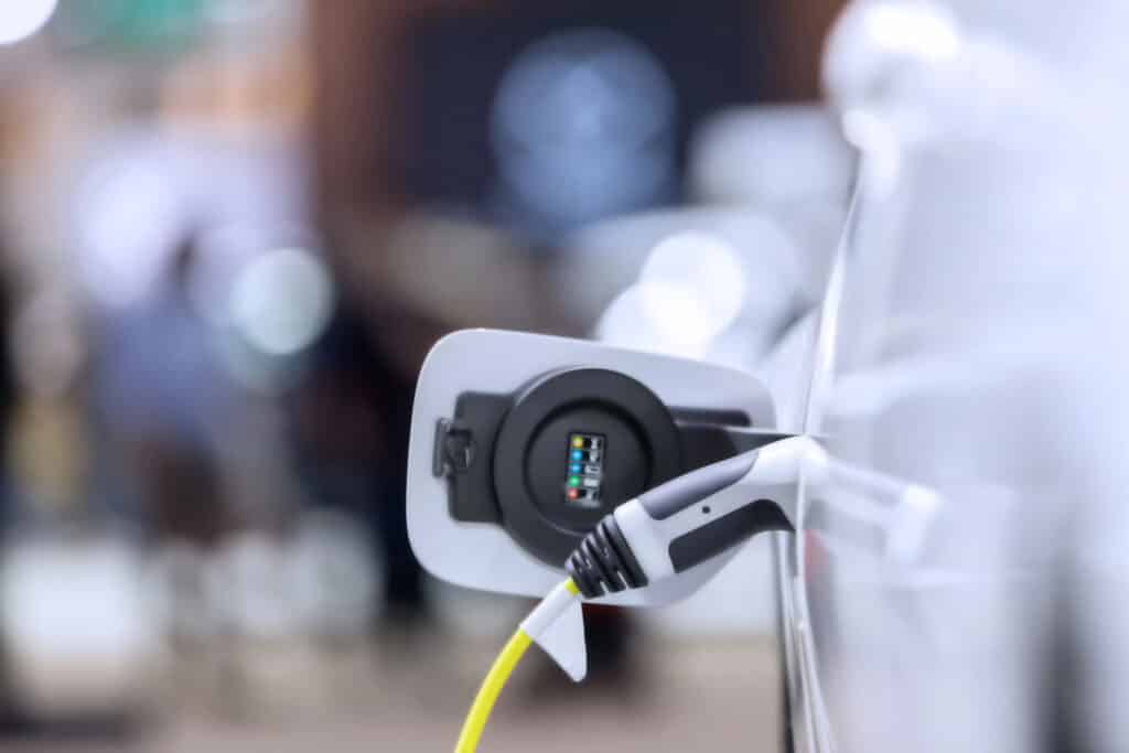 Electric vehicle charging, close-up of charger plugged into white car, blurred background.