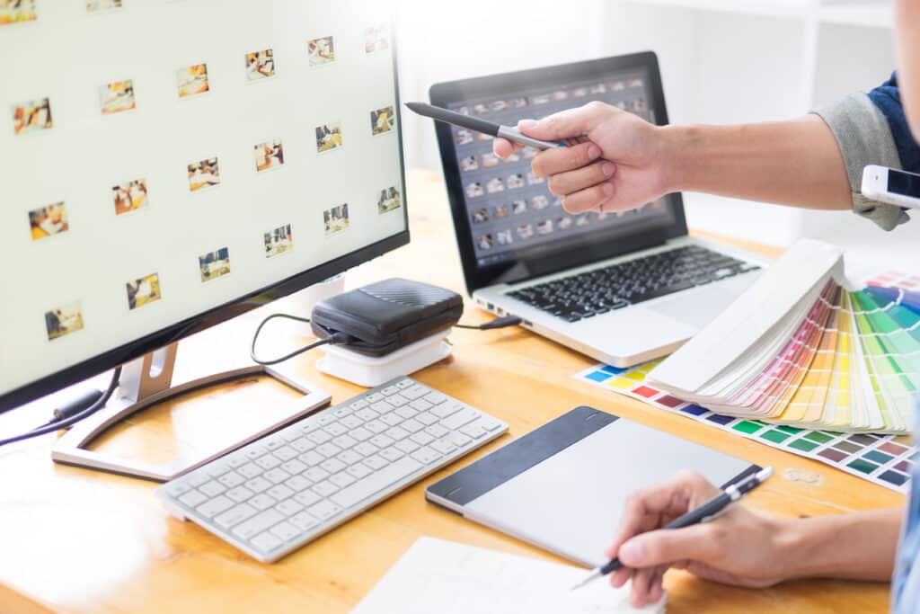 Designer working on color samples with computer screens and a stylus in a creative workspace.