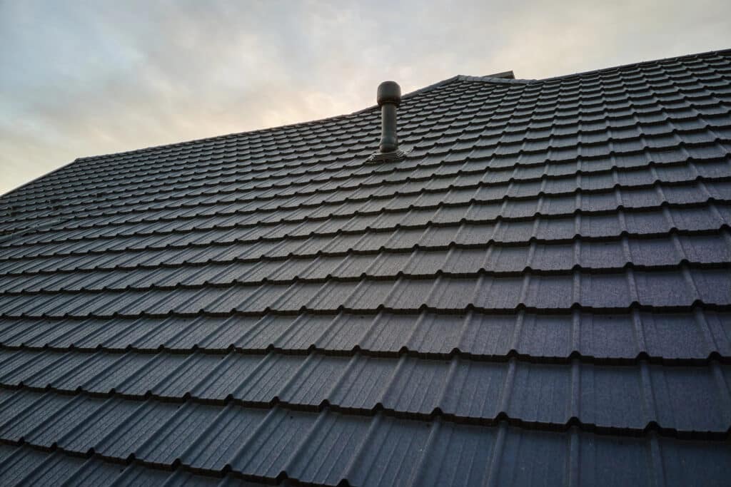 Modern gray tile roof with vent pipe against a cloudy sky.