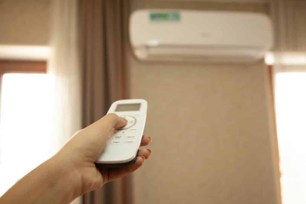 Person using remote control to operate a modern air conditioner in a cozy room setting.