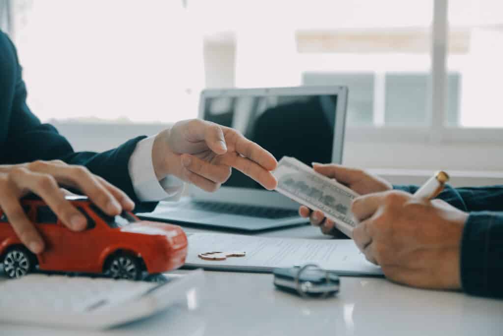 Car purchase negotiation with toy car, money, and documents on table in office setting.