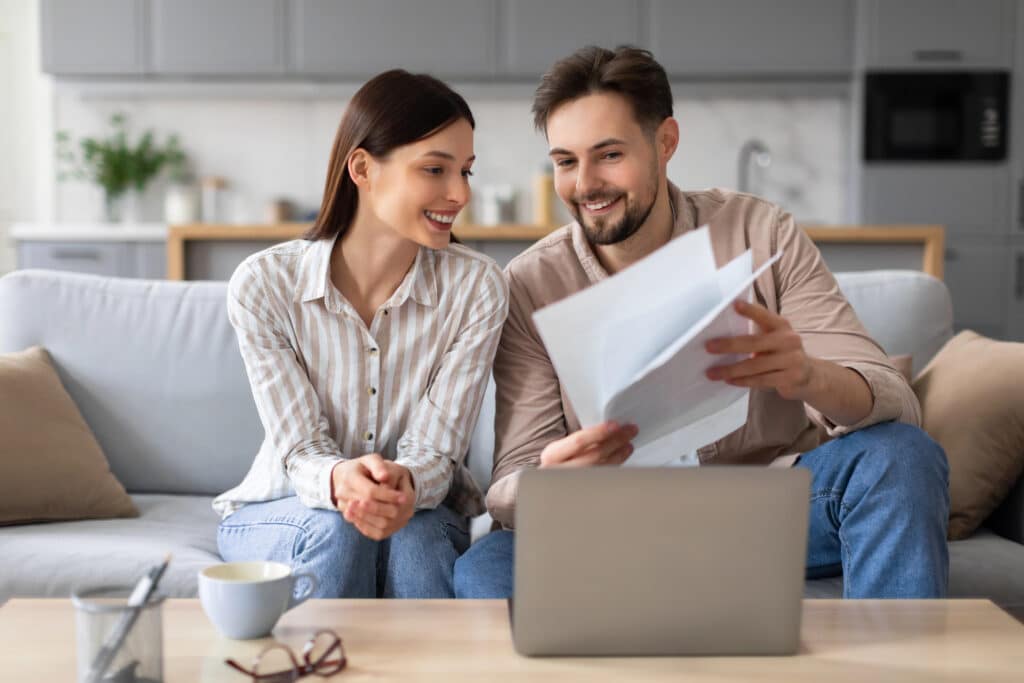 Depositphotos_704264932_XL Happy couple reviewing documents together on a couch with a laptop in a cozy living room. | Sky Rye Design Happy couple reviewing documents together on a couch with a laptop in a cozy living room.