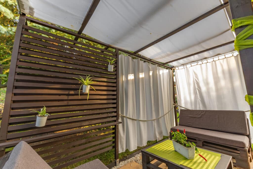 Cozy outdoor patio with a wooden privacy screen, white curtains, and potted plants.