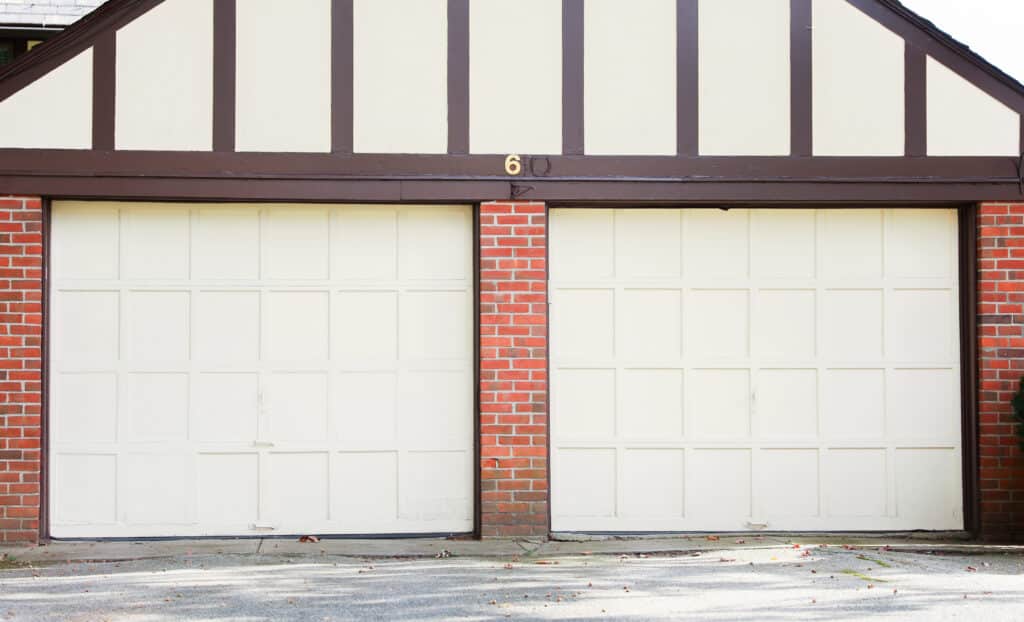 Two white garage doors with brown trim and red brick, front view of a classic residential garage.