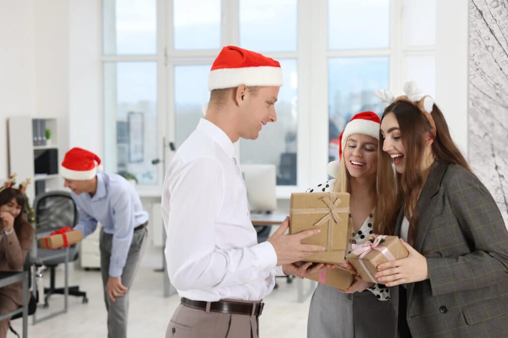 Office colleagues in Santa hats exchanging gifts at a festive holiday party with laughter and joy.