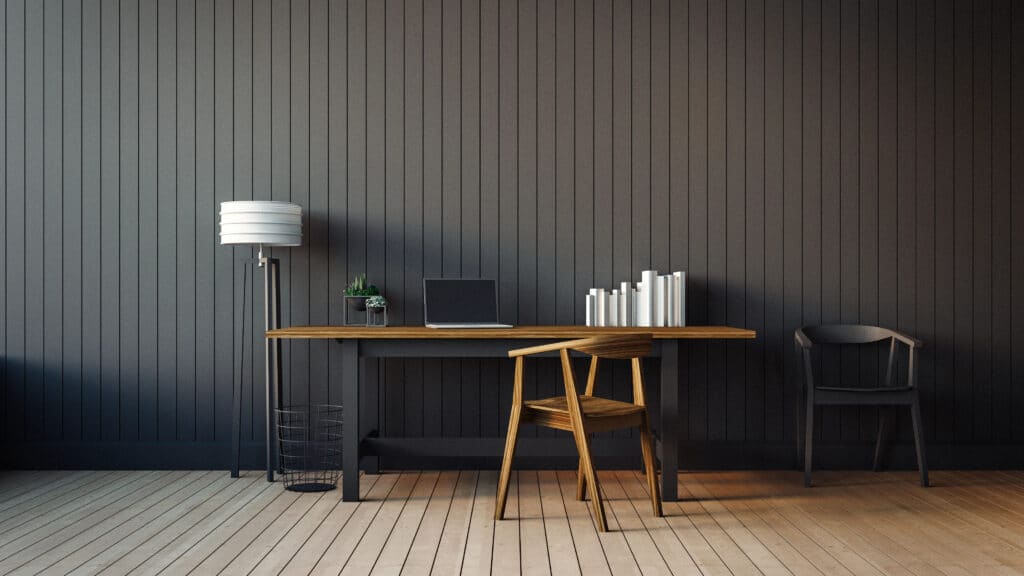 Minimalist home office with wooden desk, laptop, books, and a plant against a dark paneled wall.