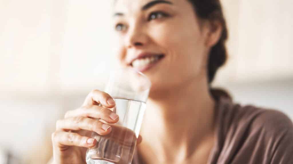 Smiling woman enjoying a refreshing glass of water for hydration.