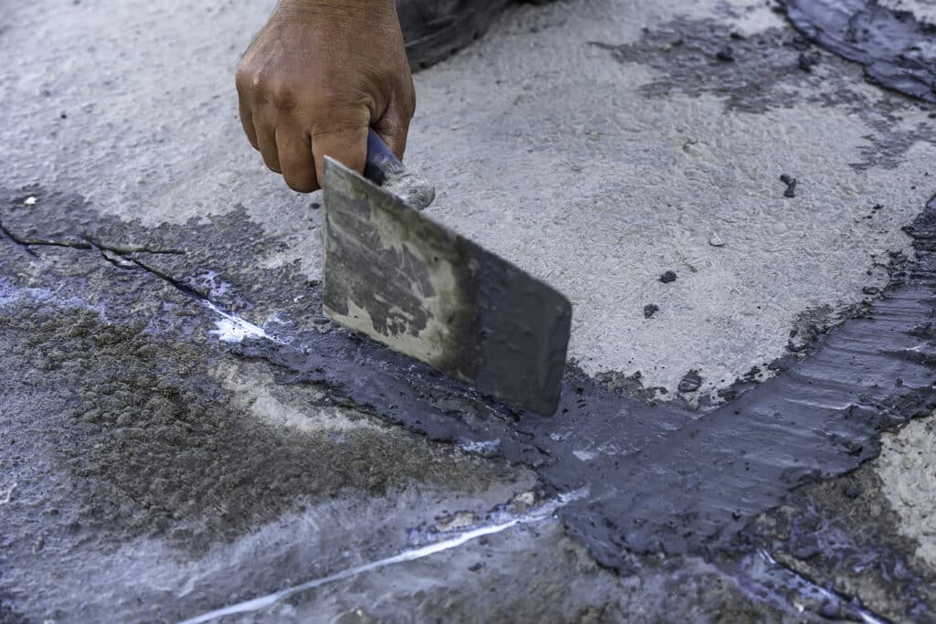 Worker using a trowel to apply sealant on concrete cracks for repair and maintenance.