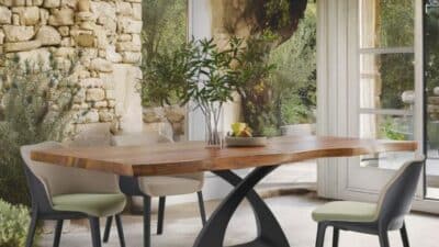 Modern dining room with a wooden table, chairs, and nature view through large windows, featuring stone walls and decor.