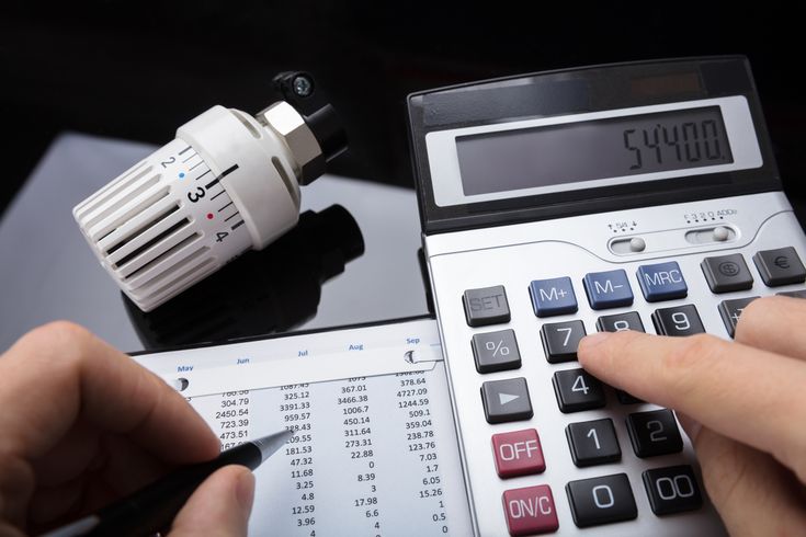 Do-It-Yourself Home Energy Audit to Cash in on Savings Person calculating heating costs with a calculator, thermostat valve, and financial spreadsheet. | Sky Rye Design Person calculating heating costs with a calculator, thermostat valve, and financial spreadsheet.