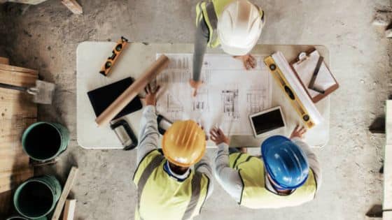 Dont Gamble on Foundation Why Hiring a Steel Pier Is Non-Negotiable Construction team reviews architectural blueprint at a job site, wearing safety gear and helmets. | Sky Rye Design Construction team reviews architectural blueprint at a job site, wearing safety gear and helmets.