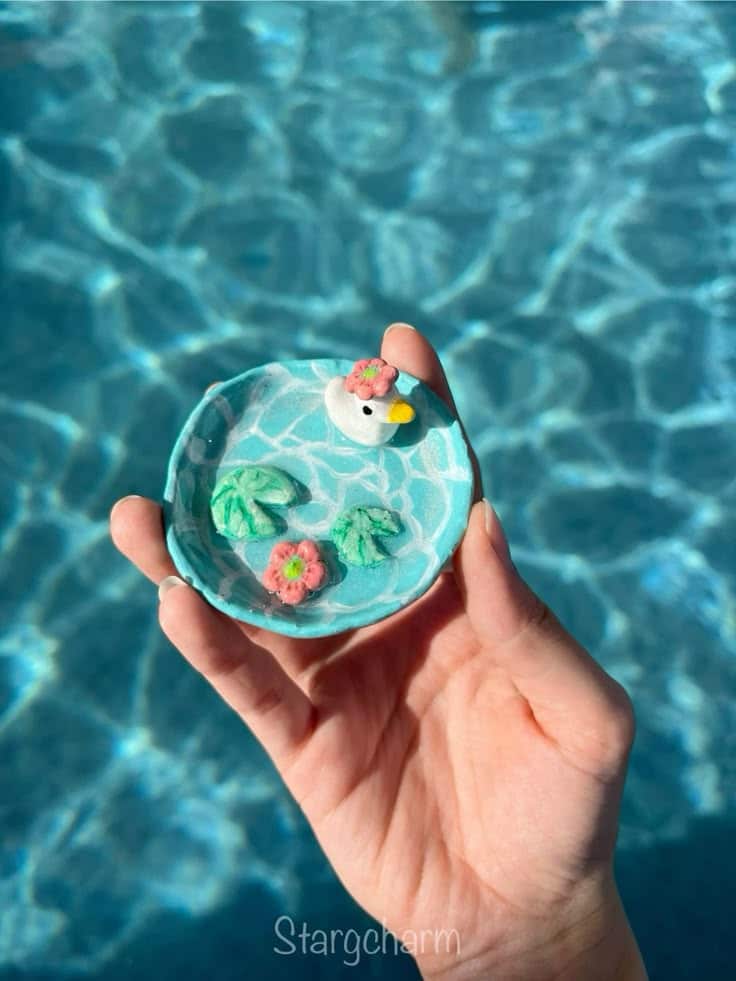 Hand holding a small ceramic dish with a cute duck and lily pads by a pool.