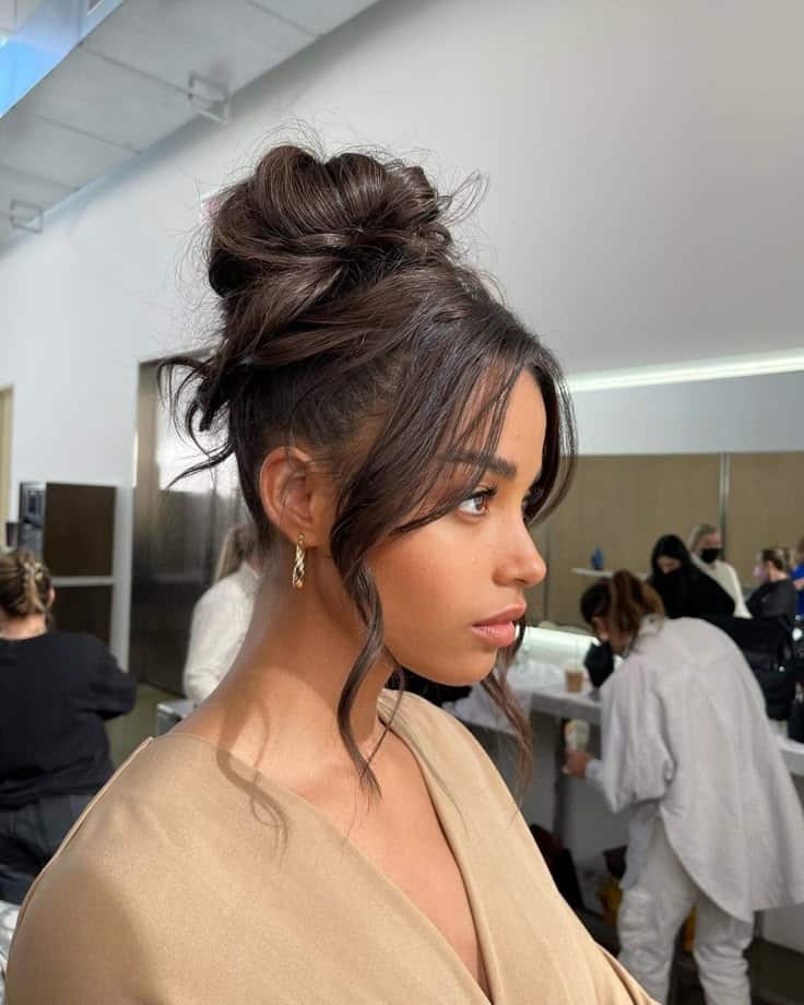 Woman with elegant updo hairstyle and makeup in a busy dressing room setting.