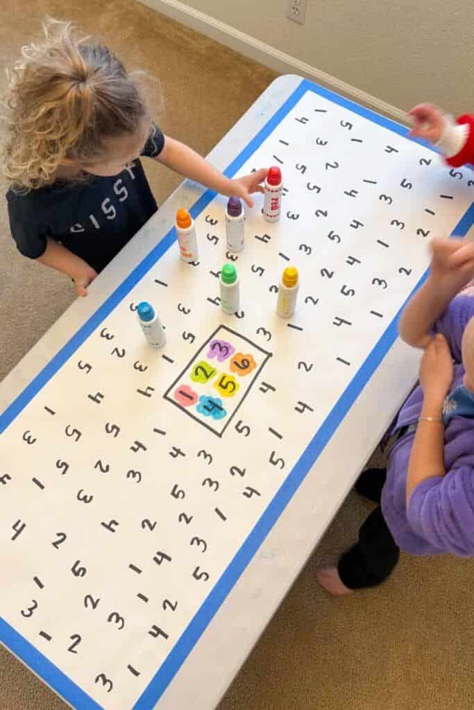 Children playing educational number matching game with colorful markers on table.