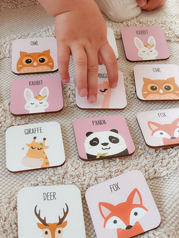 Child playing with animal-themed matching cards on a soft textured surface, featuring owl, rabbit, and fox illustrations.