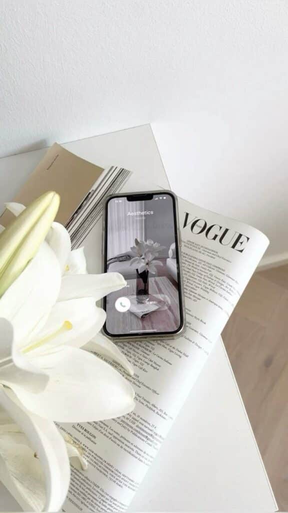 Smartphone displaying Aesthetics call on magazine page with white lily arrangement. Minimalist and elegant decor.