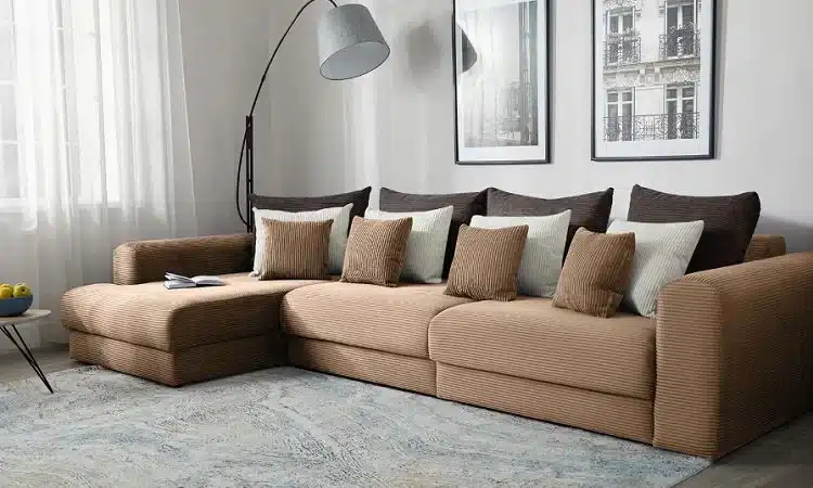 Elegant-Sofa-Upholstery-Designs-in-Dubai Stylish brown sectional sofa with cushions in a modern living room featuring framed wall art and a floor lamp. | Sky Rye Design Stylish brown sectional sofa with cushions in a modern living room featuring framed wall art and a floor lamp.