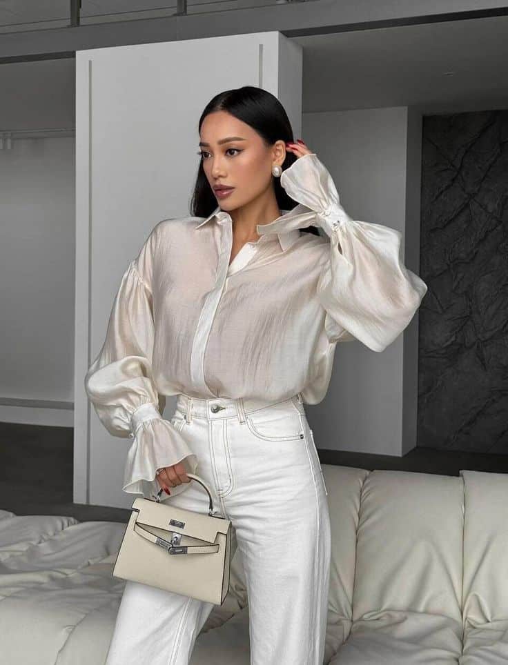 Woman in white blouse and jeans holding a handbag in a modern interior setting.