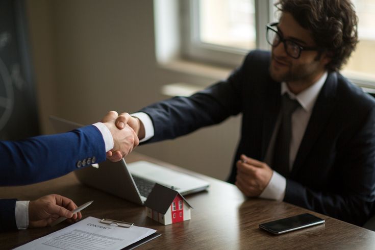 Handshake between two businessmen at a desk with paperwork and a laptop, symbolizing a successful business deal.