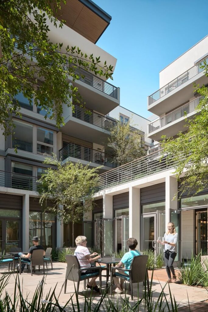 Modern apartment courtyard with people enjoying outdoor seating under a clear blue sky.