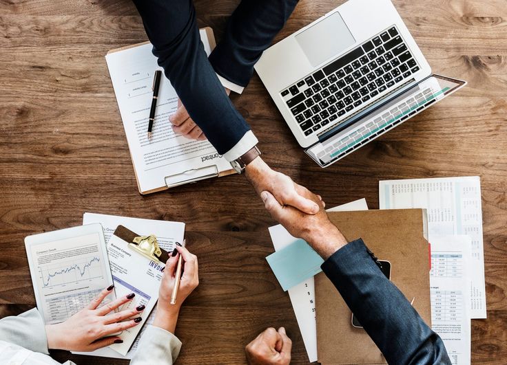 Business handshake over paperwork and laptop on a wooden desk, symbolizing successful partnership and teamwork.