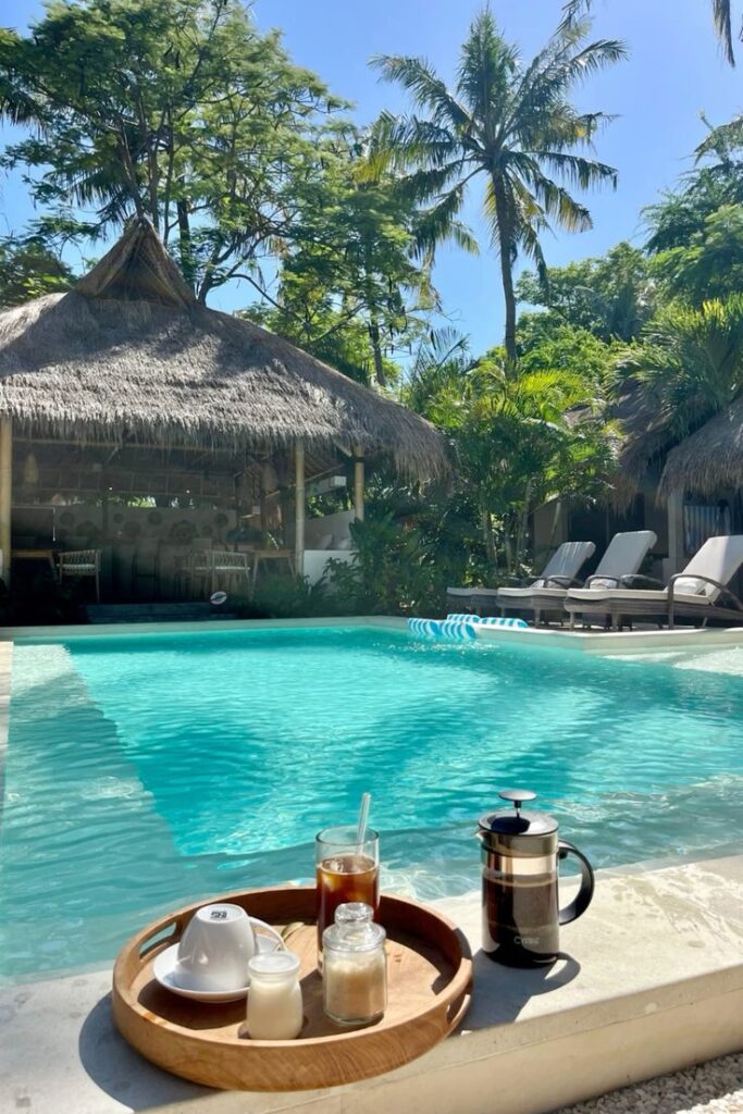 Tropical poolside with coffee tray, cozy loungers, and lush greenery under palm trees, perfect for relaxation.