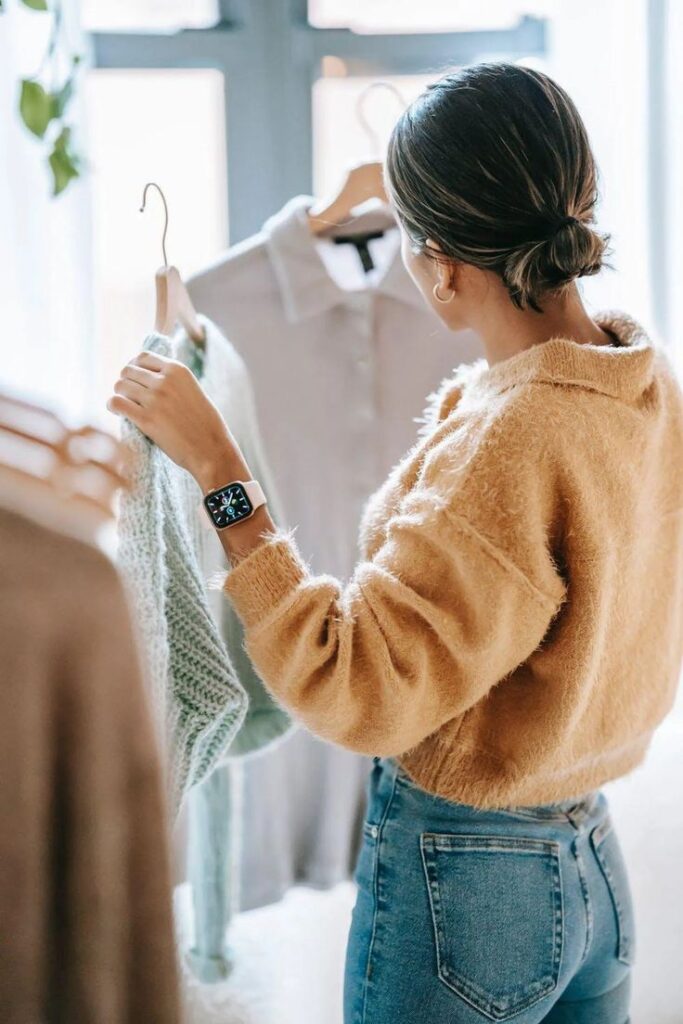 Everything You Need To Know About Minimalist Clothing Woman browsing clothes in a store, wearing a fuzzy sweater and smart watch, holding a teal knitted garment. | Sky Rye Design Woman browsing clothes in a store, wearing a fuzzy sweater and smart watch, holding a teal knitted garment.