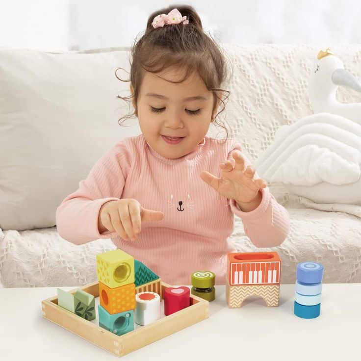 Toddler playing with colorful educational blocks, developing fine motor skills and creativity on a cozy sofa.