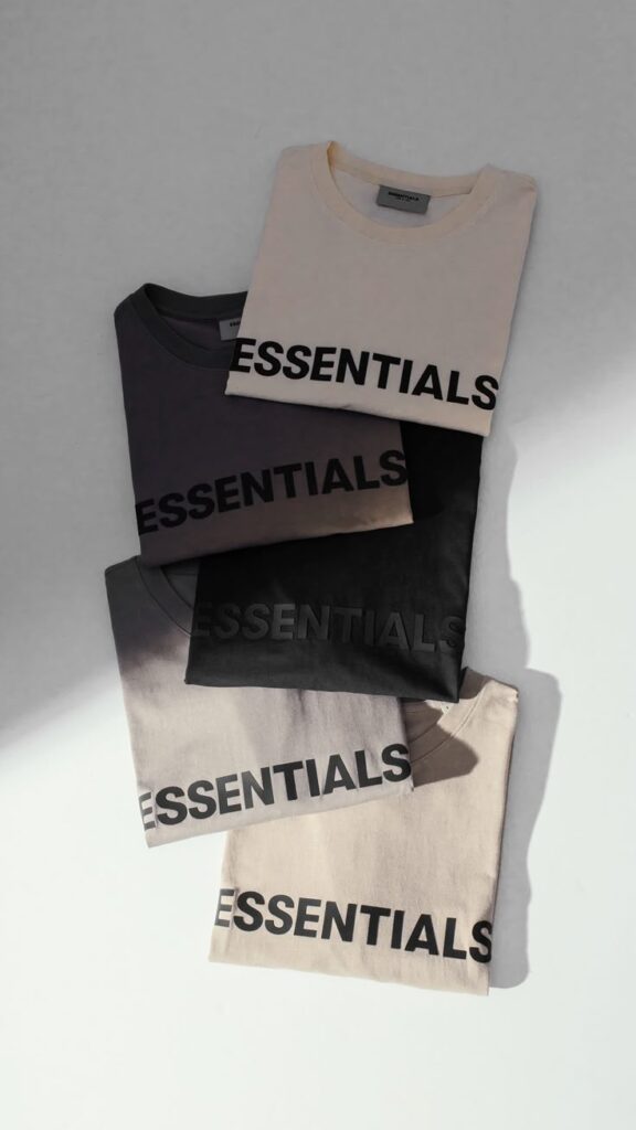 Fear of God ESSENTIALS Four folded Essentials t-shirts in neutral shades on a white surface, creating a minimalist aesthetic. | Sky Rye Design Four folded Essentials t-shirts in neutral shades on a white surface, creating a minimalist aesthetic.
