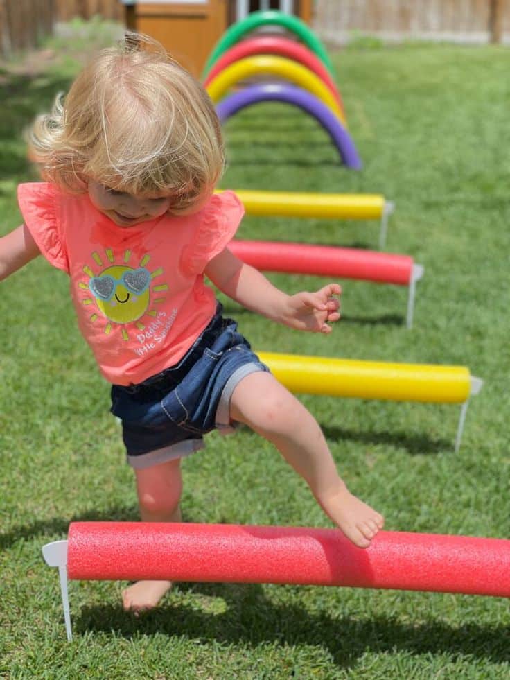 Toddler balancing on colorful foam obstacle course outdoors.