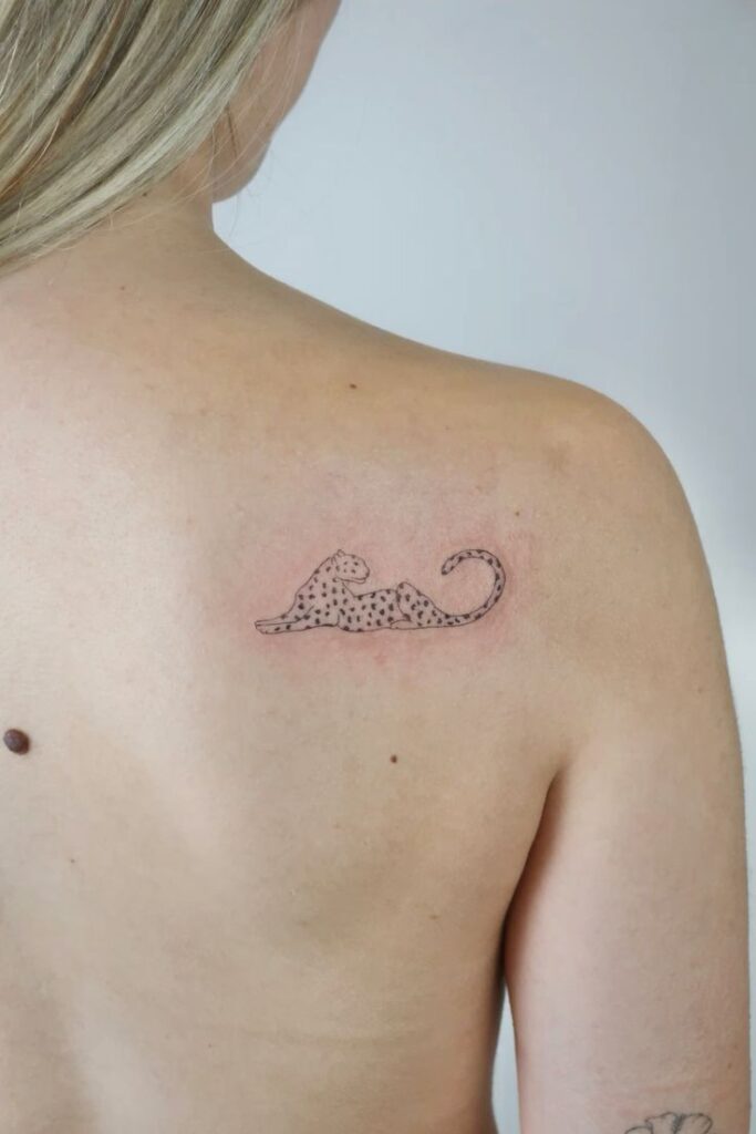 Minimalist leopard tattoo on upper back, featuring sleek lines and dots on skin.