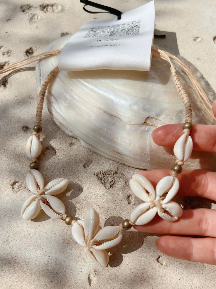 Handmade shell necklace with floral design on sandy beach, showcasing coastal style and natural craftsmanship.