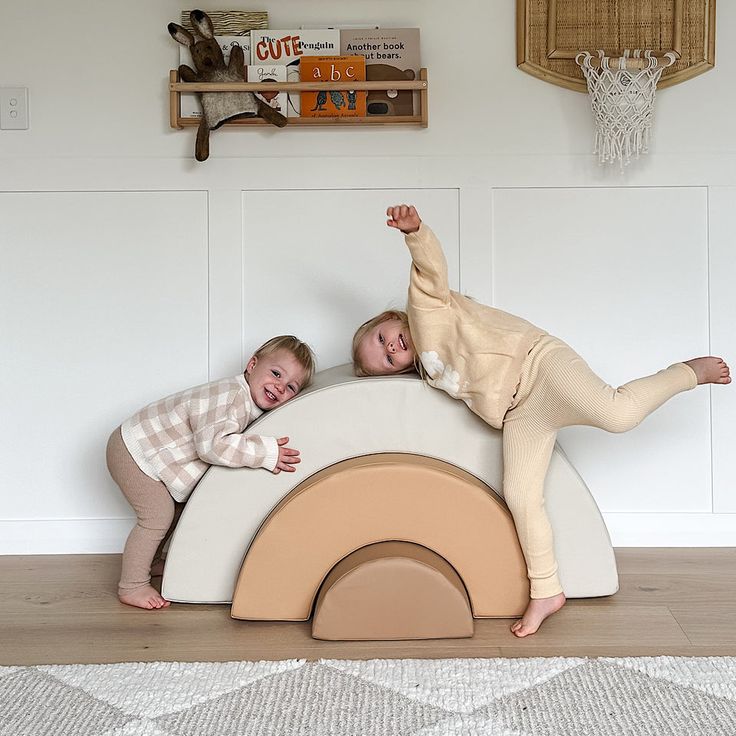 Two children playing on soft rainbow-shaped furniture in a cozy room with books and toys. Indoor Games for Kids