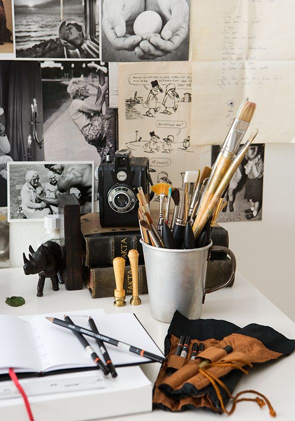Artistic workspace with brushes, vintage camera, notebooks, and photos on the wall. Creative inspiration setup.