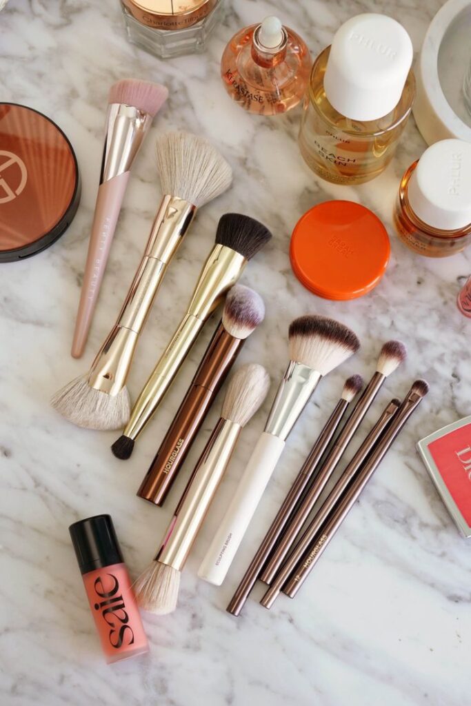 Assorted makeup brushes and cosmetics on a marble surface, featuring blush, perfume, and skincare products.