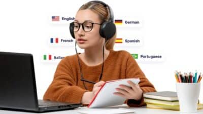 Young woman learning languages online, wearing headphones, taking notes, and using a laptop with various language flags displayed.
