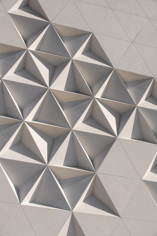 Modern geometric architectural facade with 3D triangular patterns in soft light gray.