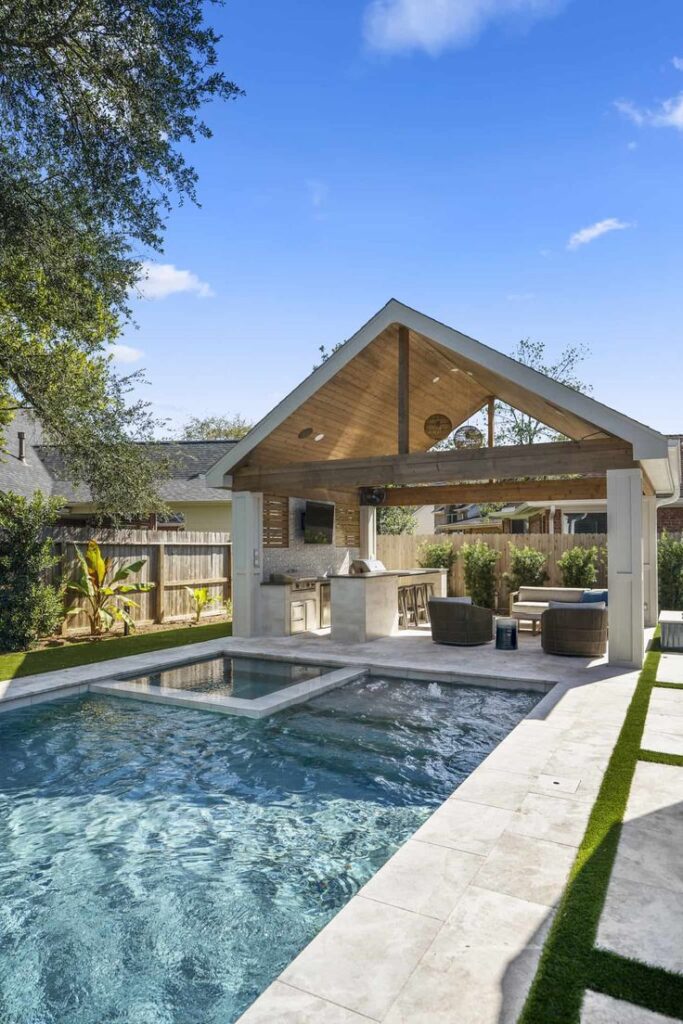 Modern backyard with pool, outdoor kitchen, and lounge area under a pergola on a sunny day.