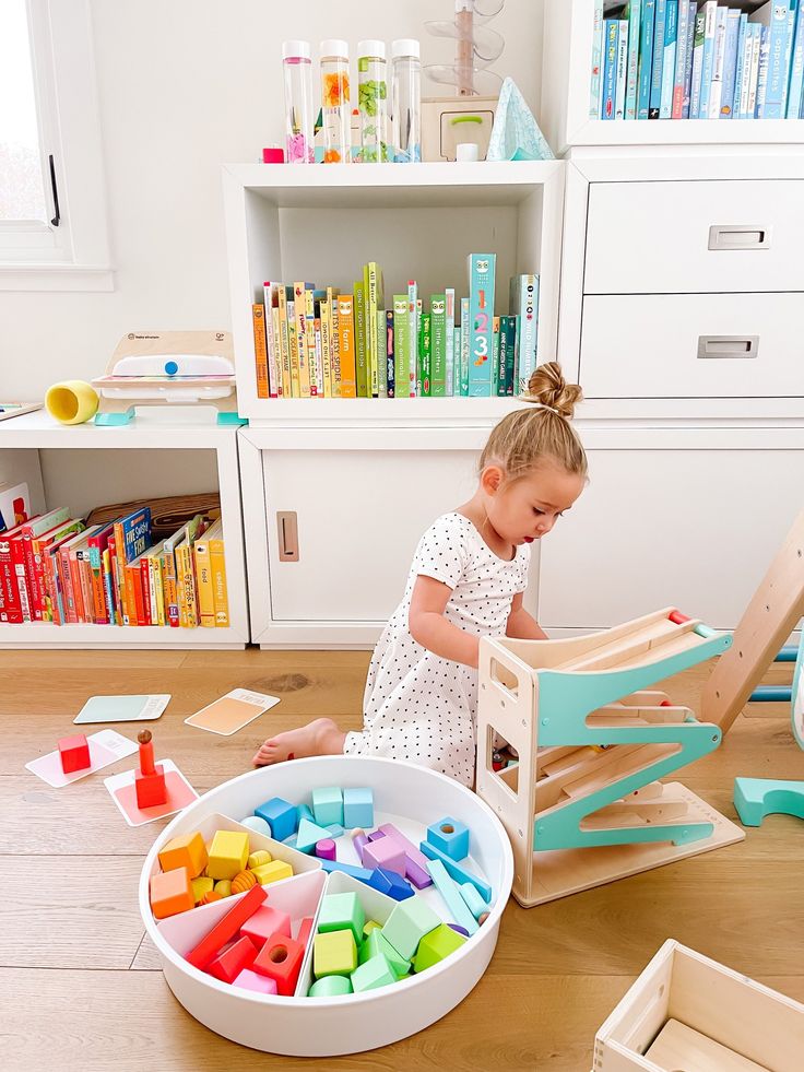 A child playing with colorful wooden blocks in a bright, organized playroom with bookshelves.