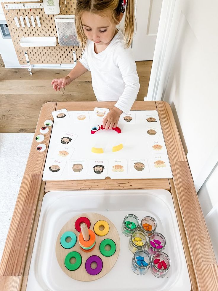 Young child playing with educational toys at a table, using colorful shapes and cards for learning activities.