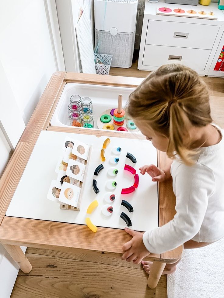 Child playing with colorful educational toys on a wooden table in a bright playroom.