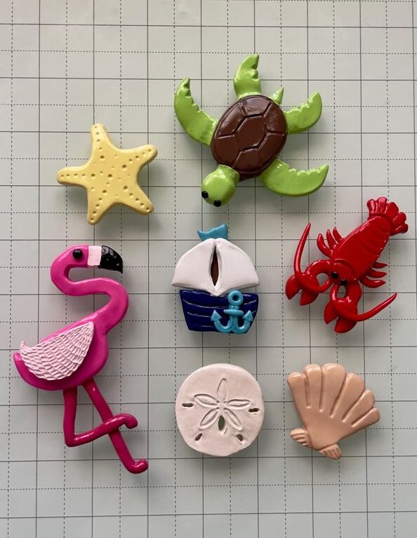 Colorful nautical-themed magnets including turtle, flamingo, lobster, starfish, sailboat, shell, and sand dollar on grid.