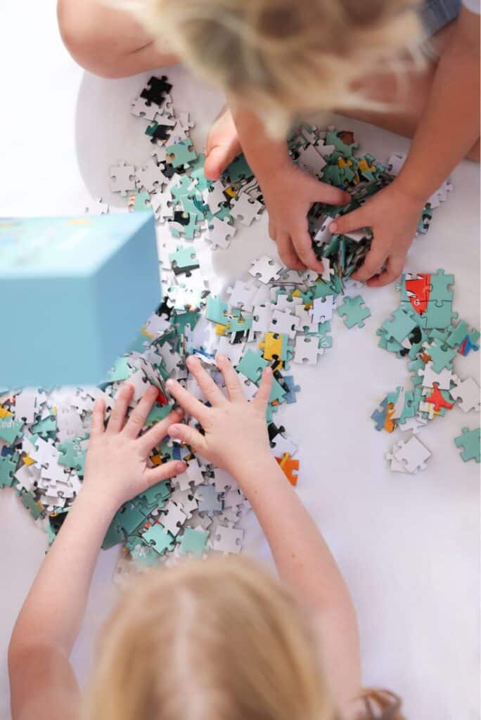 Children assembling a colorful jigsaw puzzle on a white surface, focusing on teamwork and creativity.