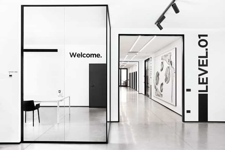 Modern office interior with minimalist design, featuring glass partitions and monochrome art, labeled Welcome and LEVEL 01.