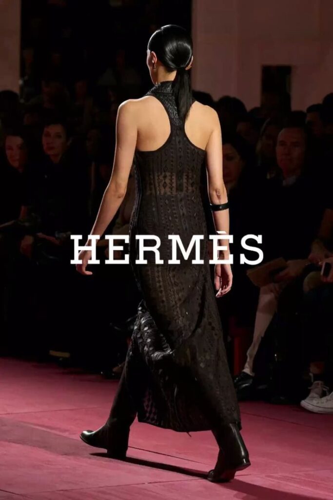 Model in a black Hermes dress on a runway, showcasing elegant fashion design.