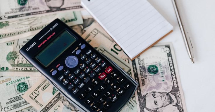 Calculator on dollar bills with notepad and pen, representing finance and budgeting concepts.